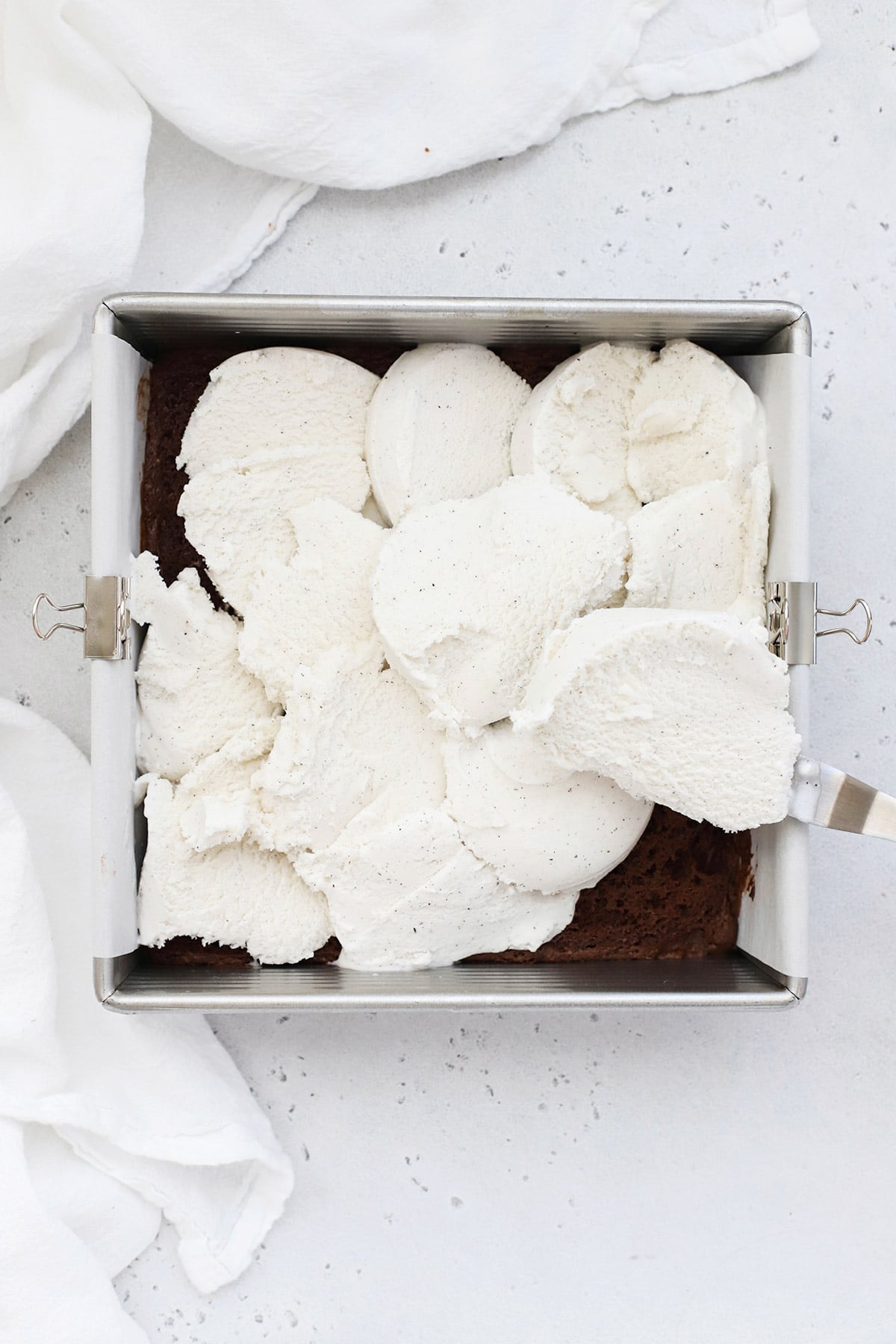 Scooping ice cream onto gluten-free brownies to make gluten-free brownie ice cream sandwiches