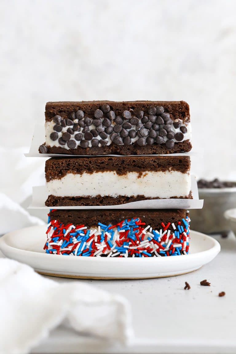 Three gluten-free brownie ice cream sandwiches on a plate. One is rolled in chocolate chip and one is rolled in red, white, and blue sprinkles