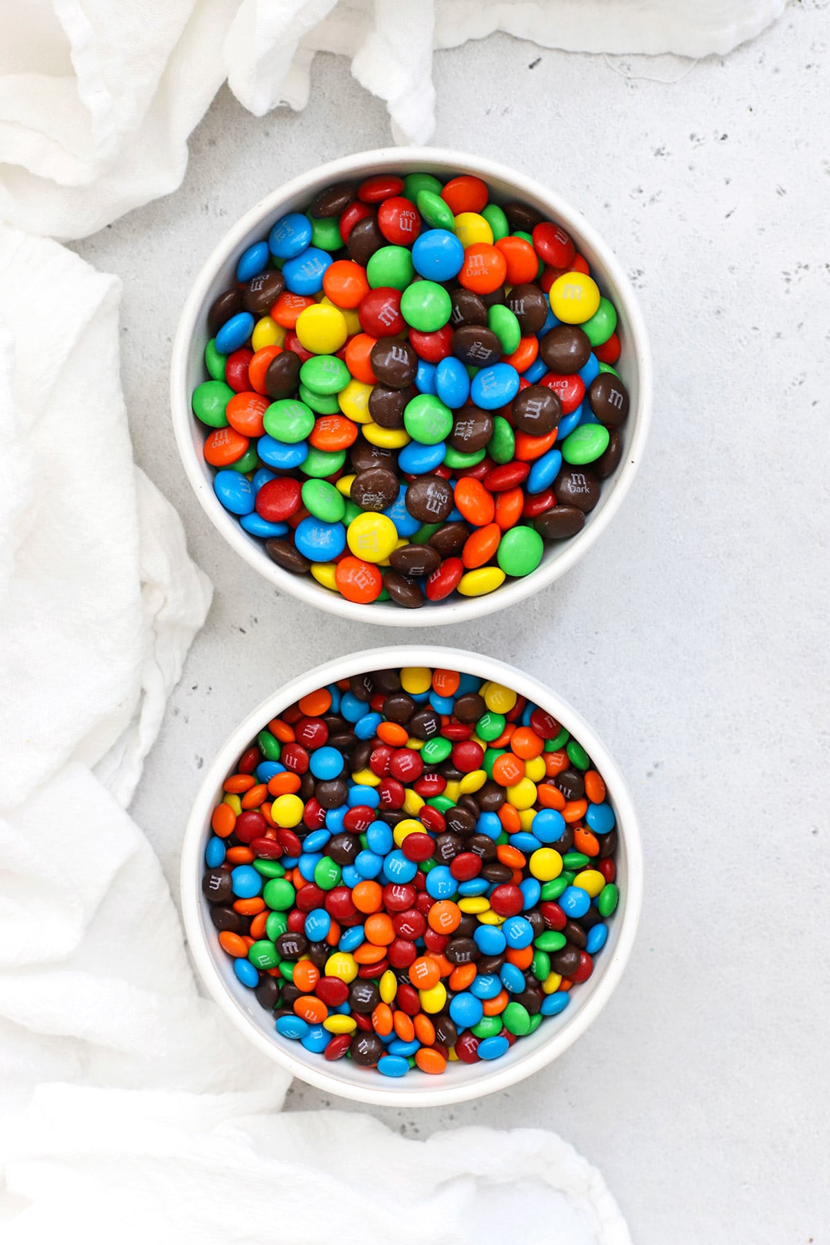Overhead view of two bowls of m&ms--one bowl of mini m&ms and one bowl of m&ms