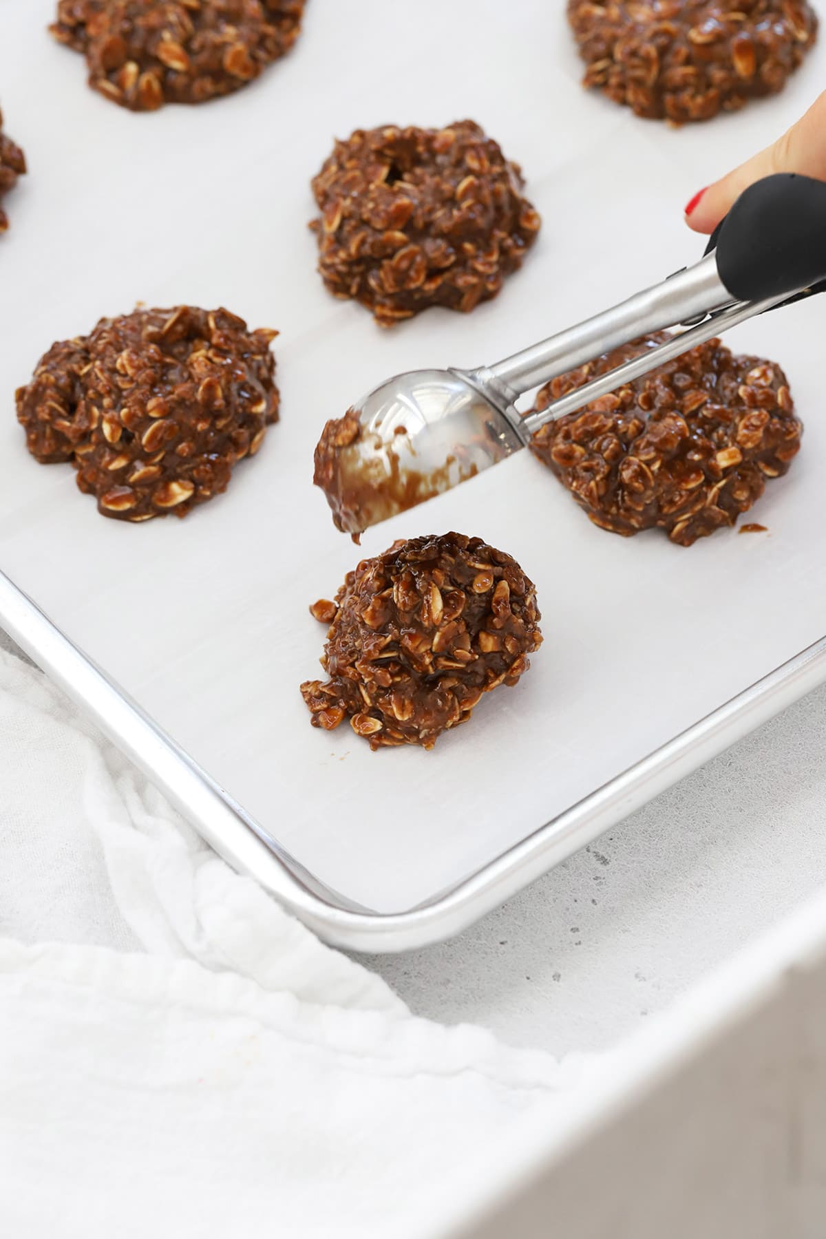 Scooping gluten-free no-bake cookies onto a baking sheet lined with parchment