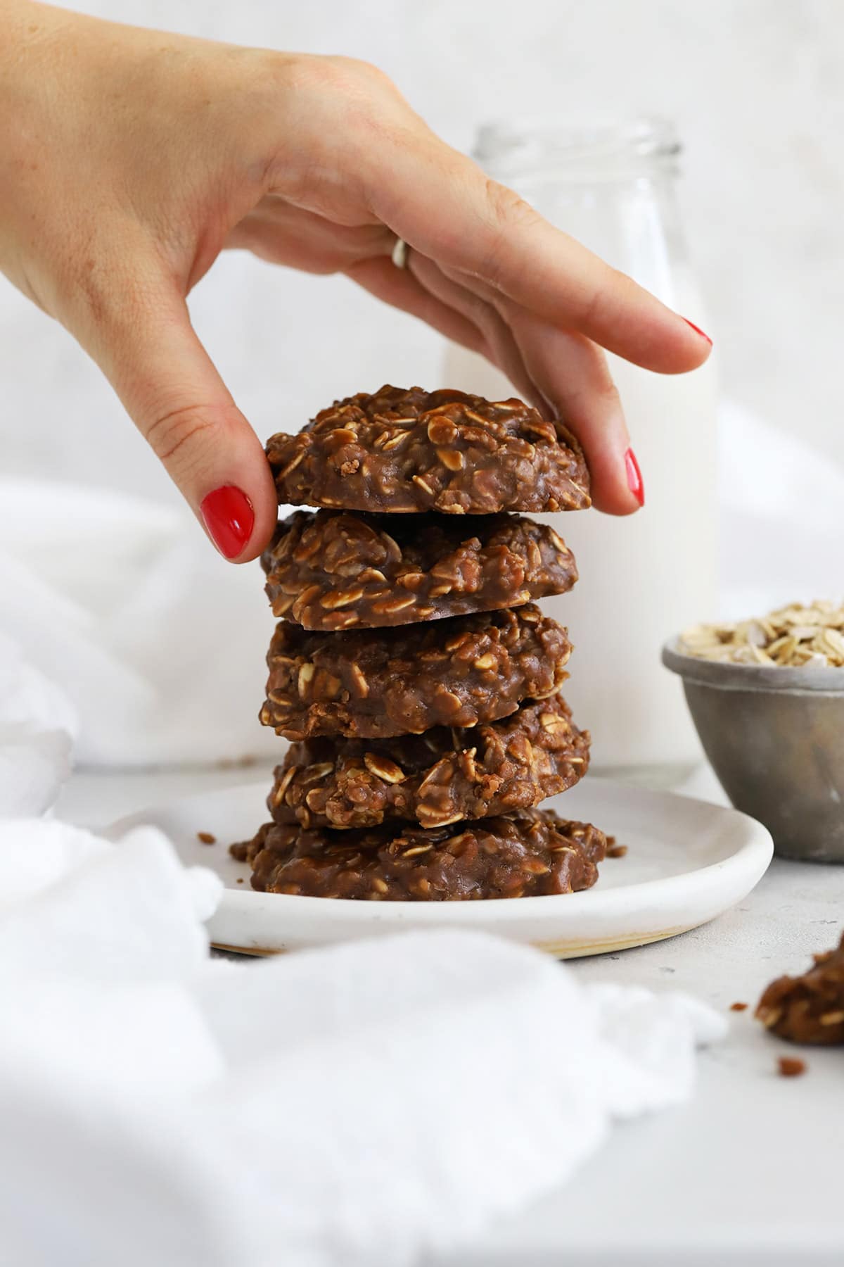 A stack of five gluten-free no-bake cookies on a white plate with a bottle of milk in the background