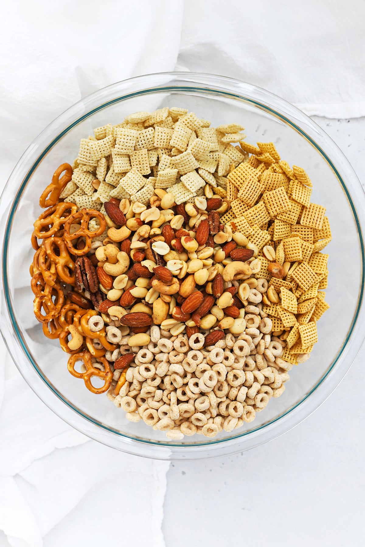 Combining gluten-free pretzels, Chex cereal, cheerios, and mixed nuts to make savory gluten-free Chex mix
