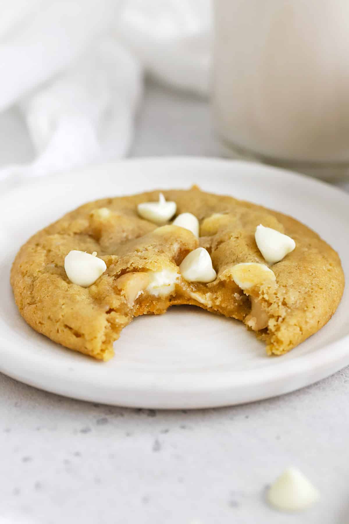 Front view of a gluten-free white chocolate macadamia cookie with a bite taken out of it
