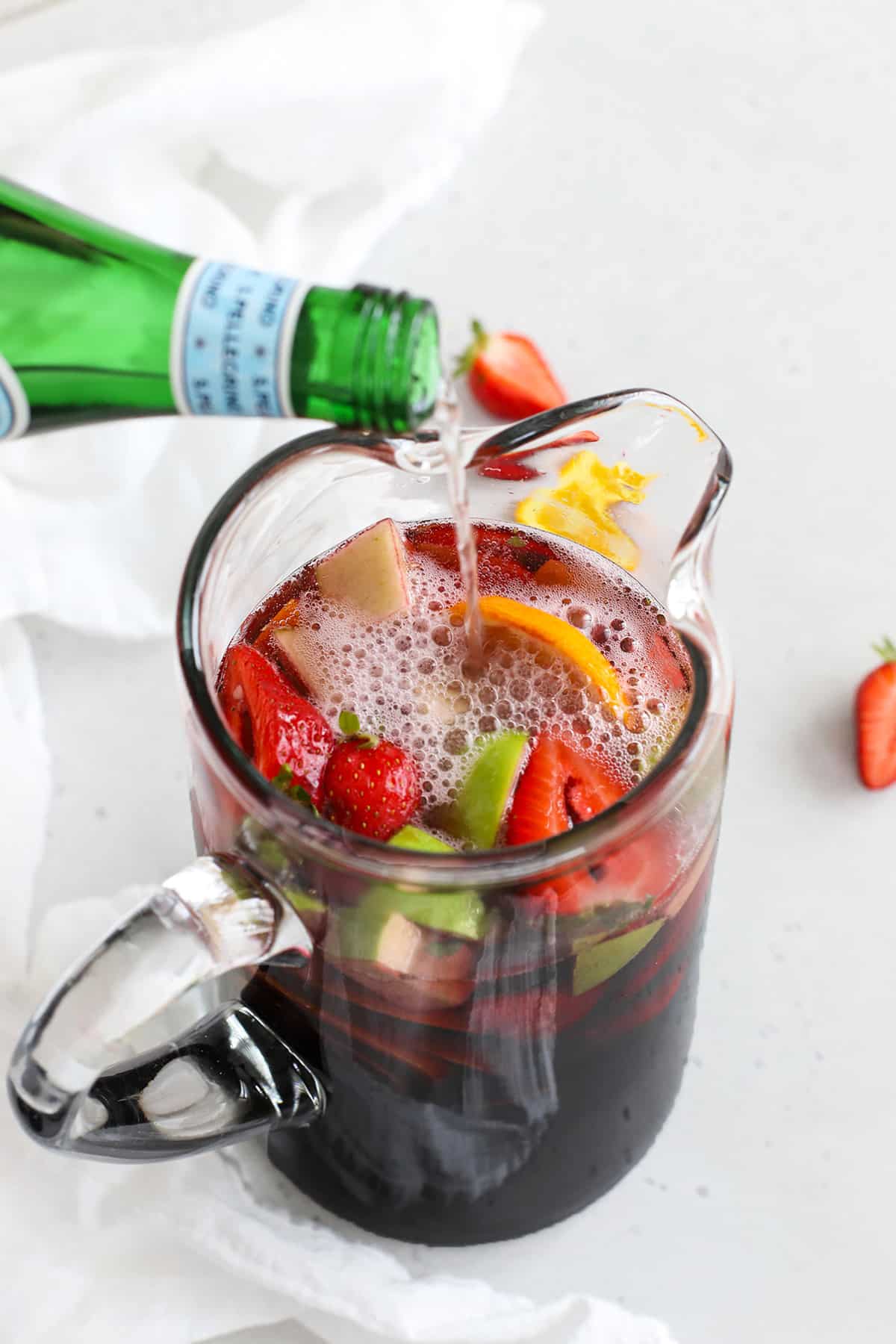 Pouring sparkling water into a pitcher of non-alcoholic sangria
