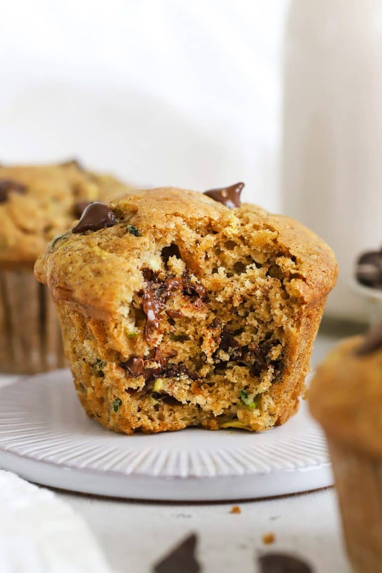 Front view of a gluten-free chocolate chip zucchini muffin with a bite out of it, revealing how moist and fluffy it is inside