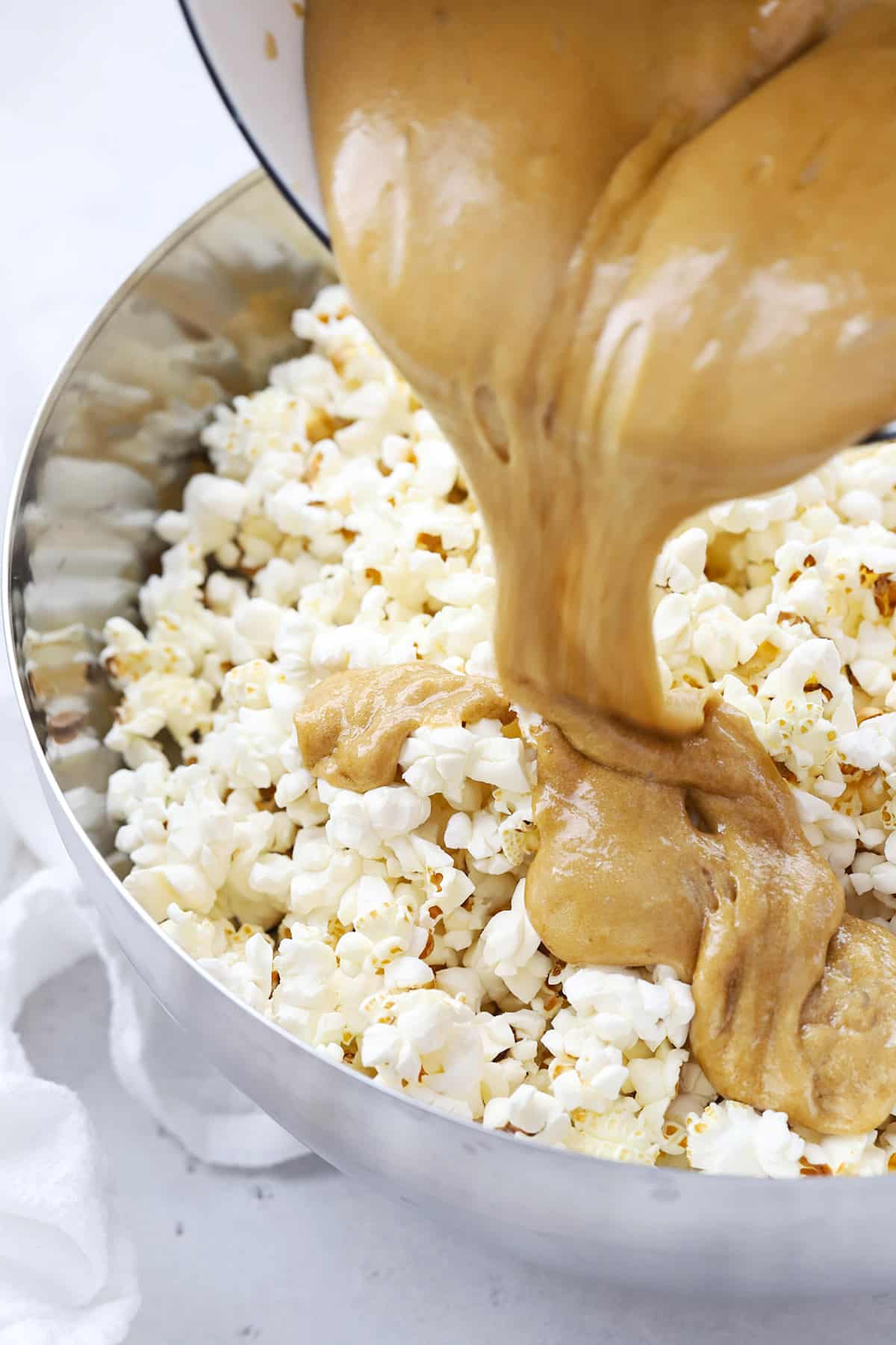 Pouring caramel sauce over popcorn in a large metal bowl