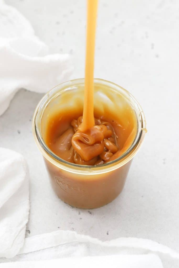 Pouring thick homemade caramel sauce into a jar