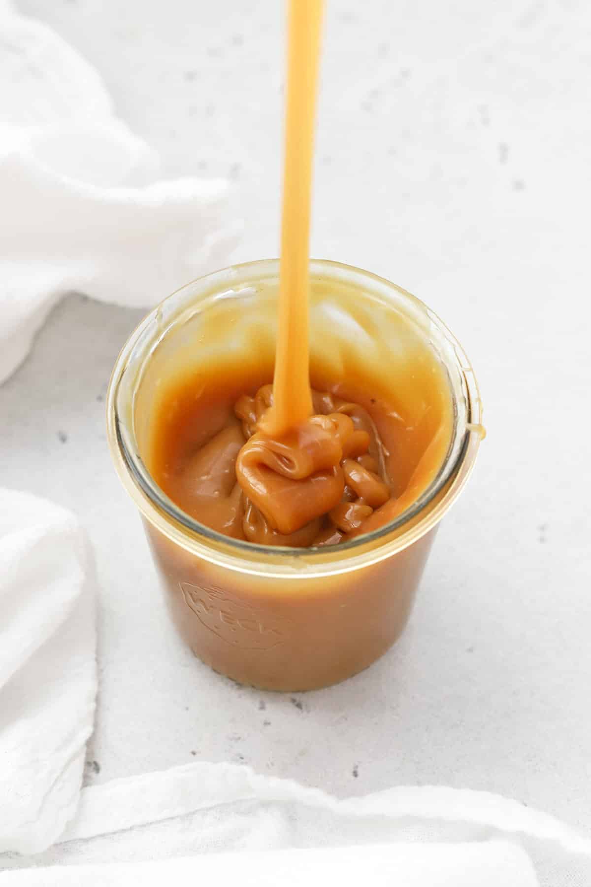 Pouring thick homemade caramel sauce into a jar