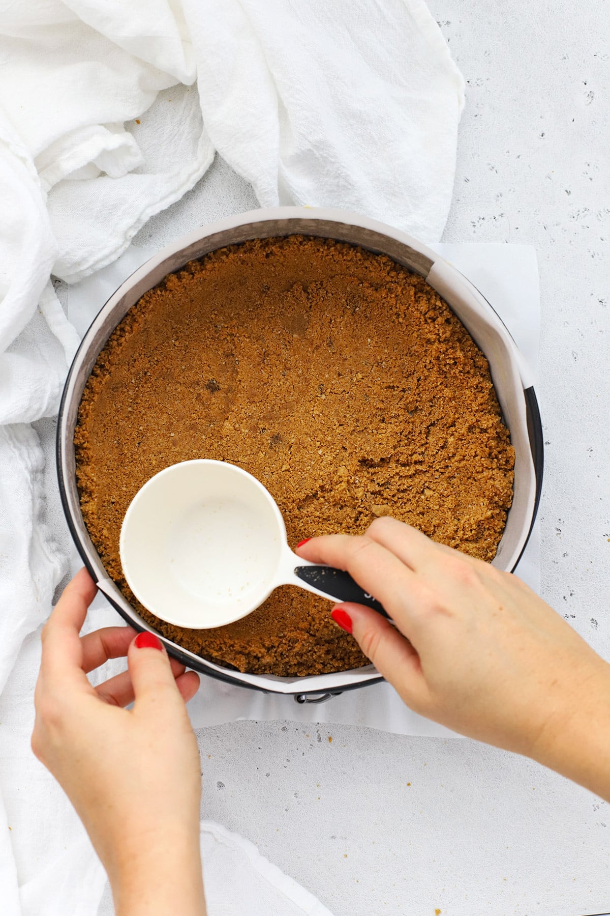 Patting gluten-free graham cracker crust into a parchment lined springform pan