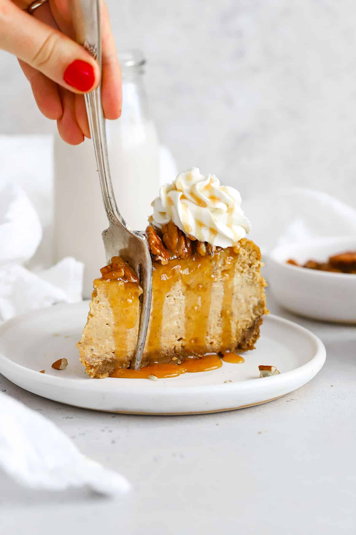 front view of a slice of gluten-free pumpkin cheesecake topped with toasted pecans, caramel sauce and whipped cream