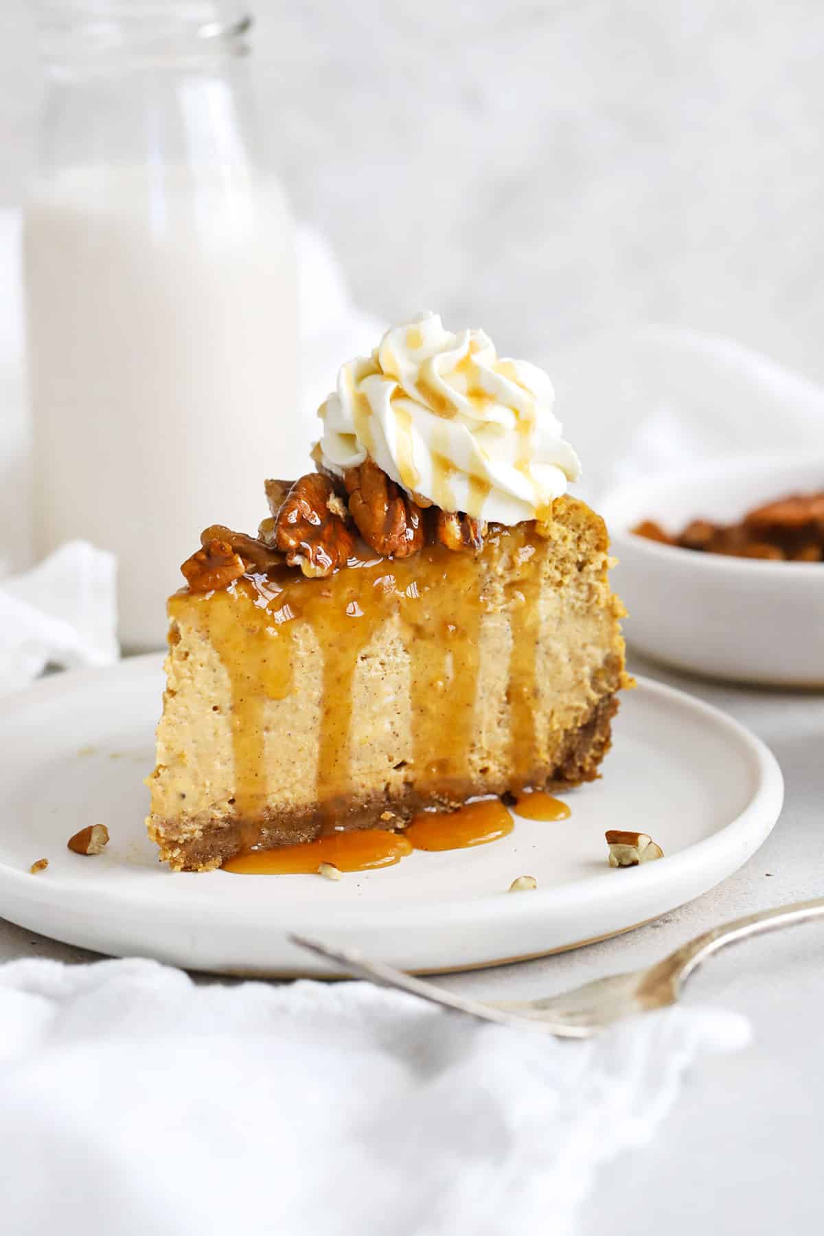front view of a slice of gluten-free pumpkin cheesecake topped with toasted pecans, caramel sauce and whipped cream