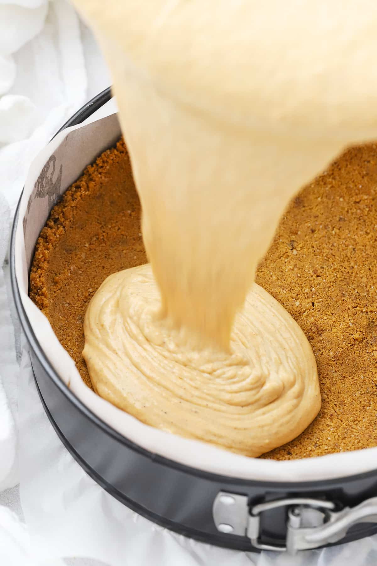 Pouring pumpkin cheesecake filling into a gluten-free graham cracker crust