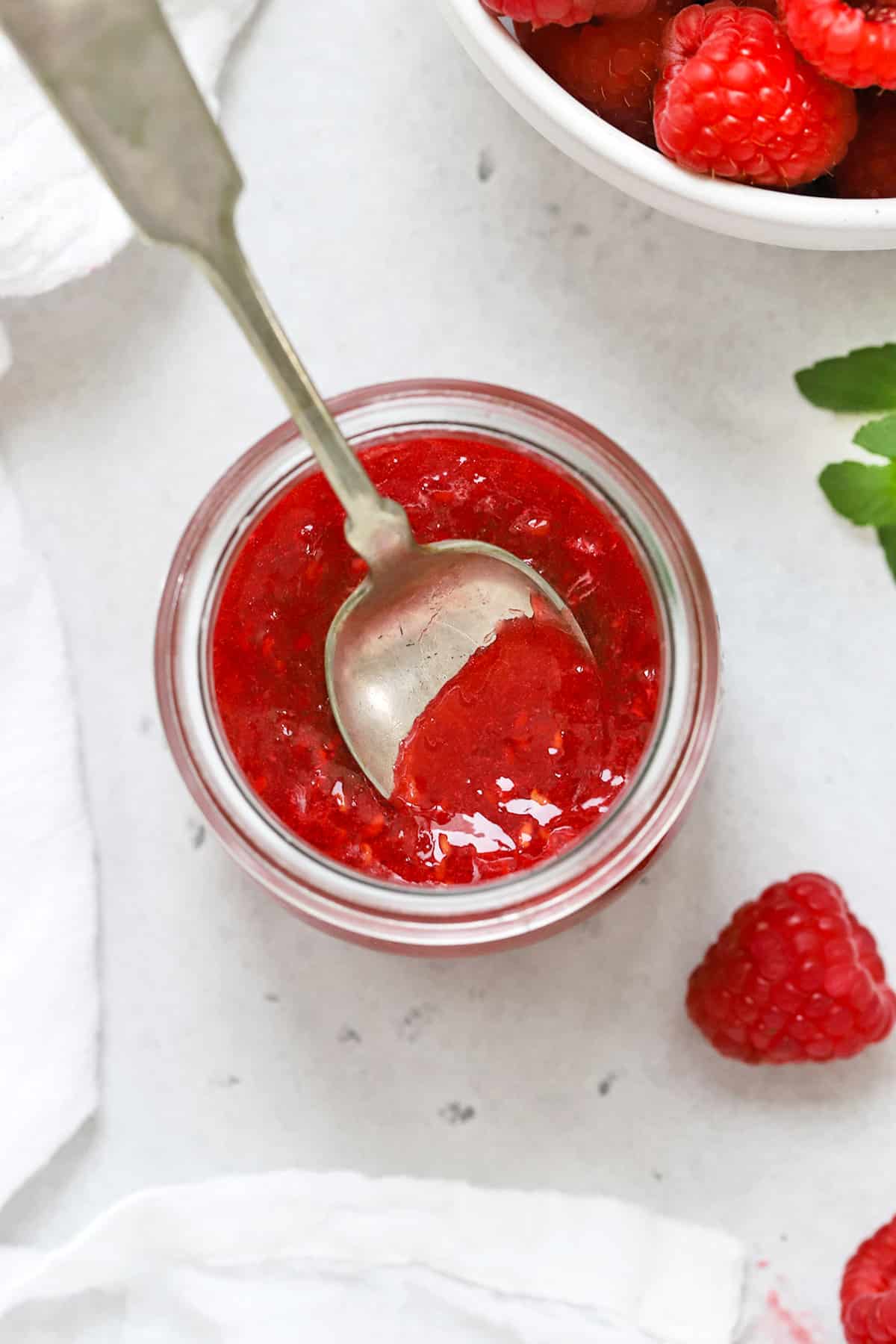 Overhead view of a jar of raspberry freezer jam with a spoon in it