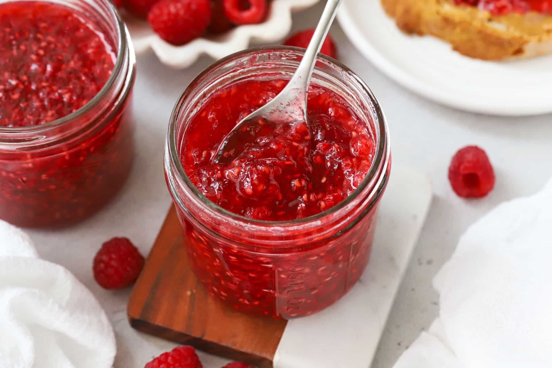 Spoon dipping into jars of low sugar raspberry freezer jam