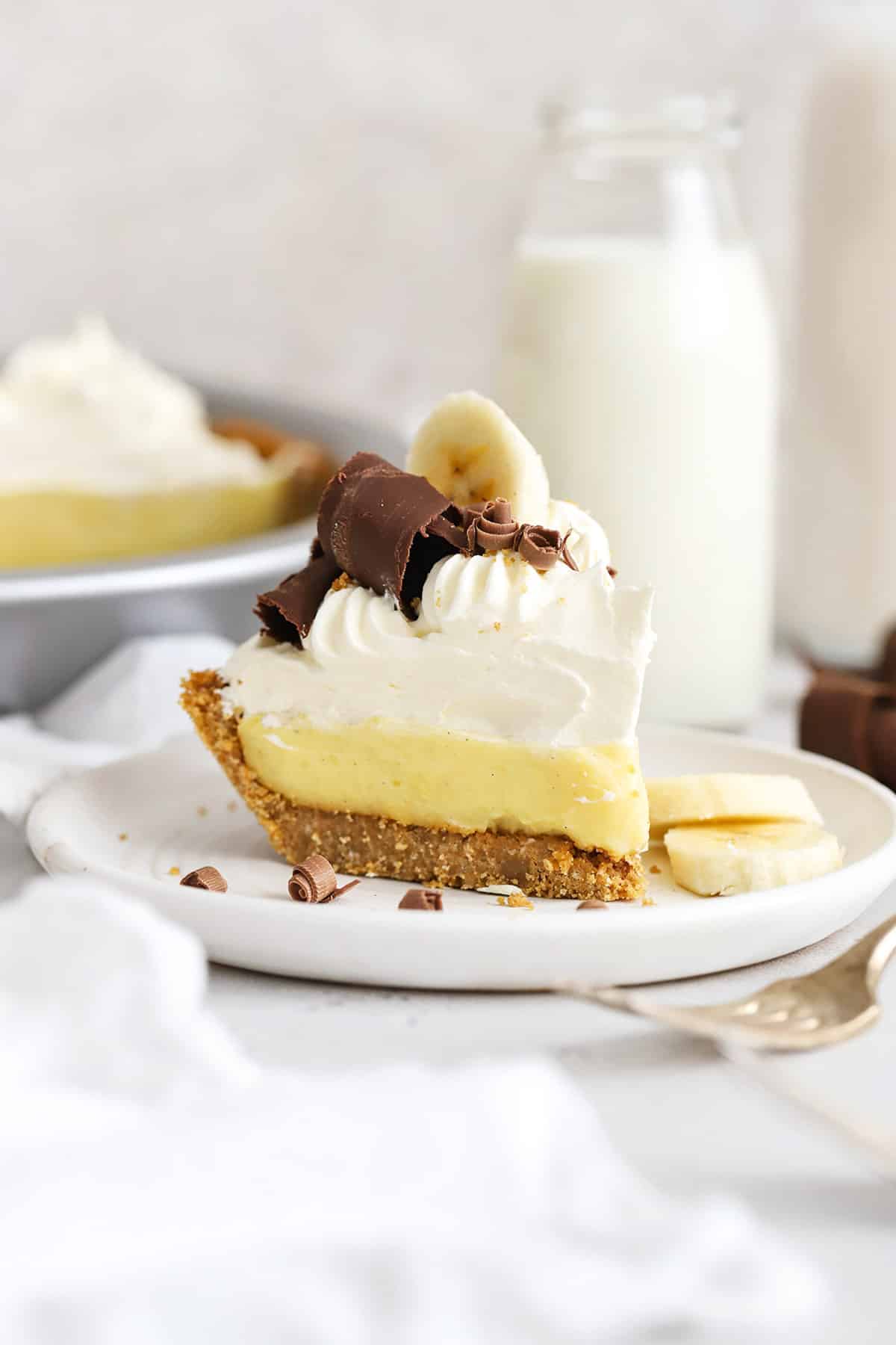 Front view of a slice of gluten-free banana cream pie topped with whipped cream and chocolate curls