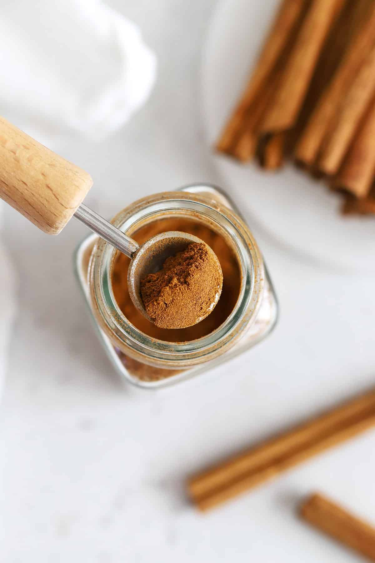Overhead view into a jar of ground cinnamon with cinnamon sticks in the background