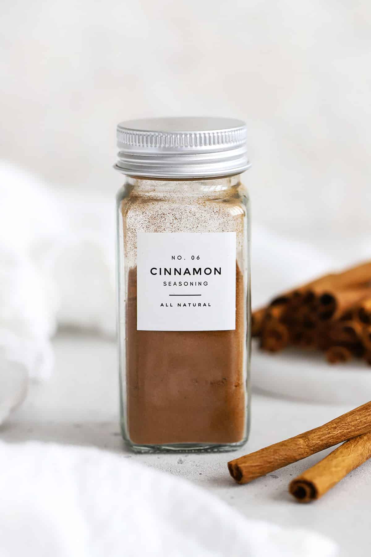 Front view of a jar of ground cinnamon with cinnamon sticks in the background