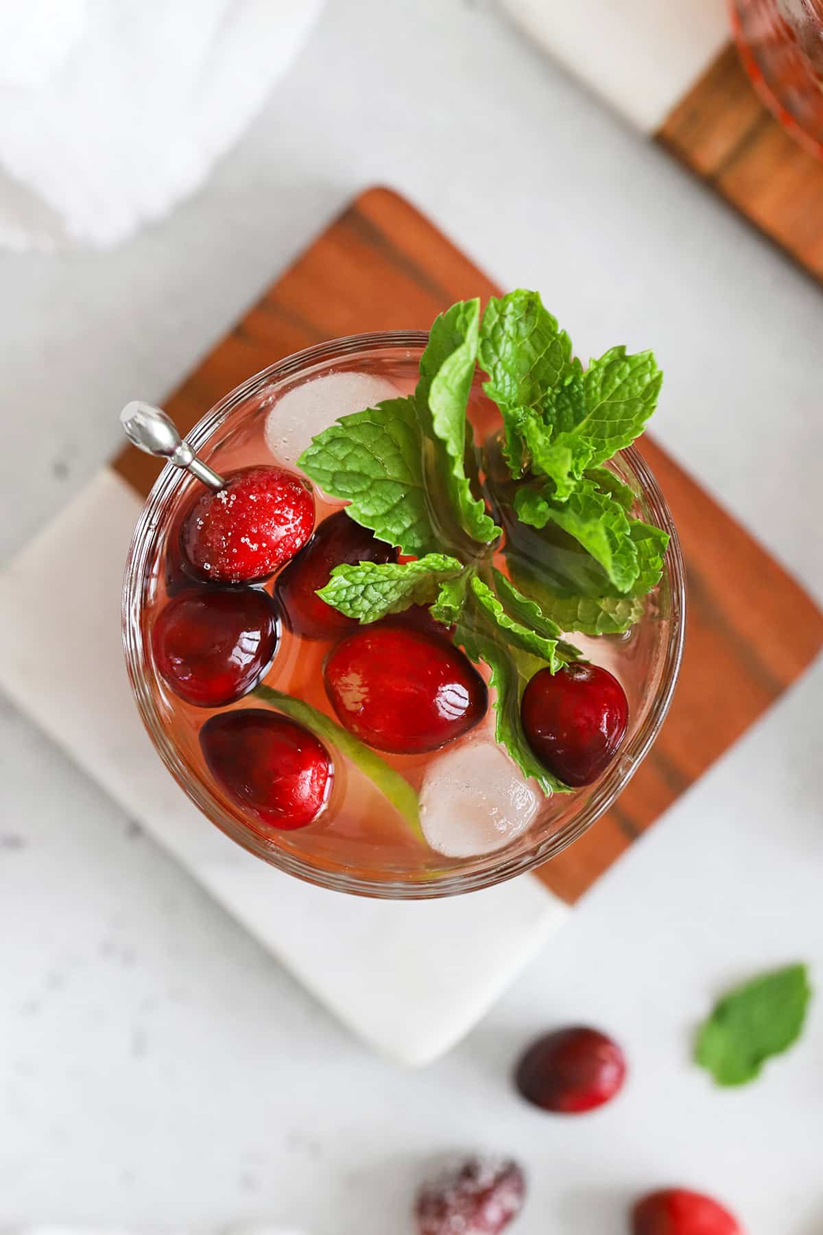 Overhead view of a cranberry mocktail in an embossed glass topped with sugared cranberries, lime slices, and a sprig of fresh mint