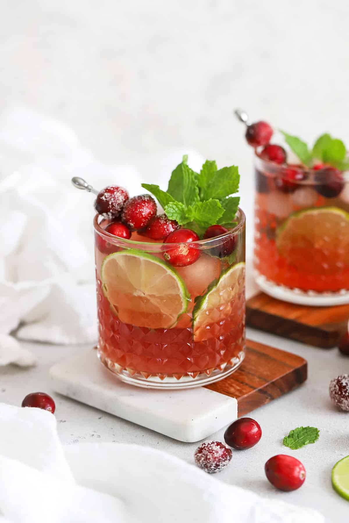 Front view of cranberry lime mocktails in embossed glasses topped with sugared cranberries, lime slices, and fresh mint