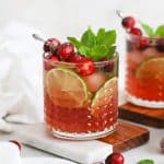 Front view of cranberry lime mocktails in embossed glasses topped with sugared cranberries, lime slices, and fresh mint