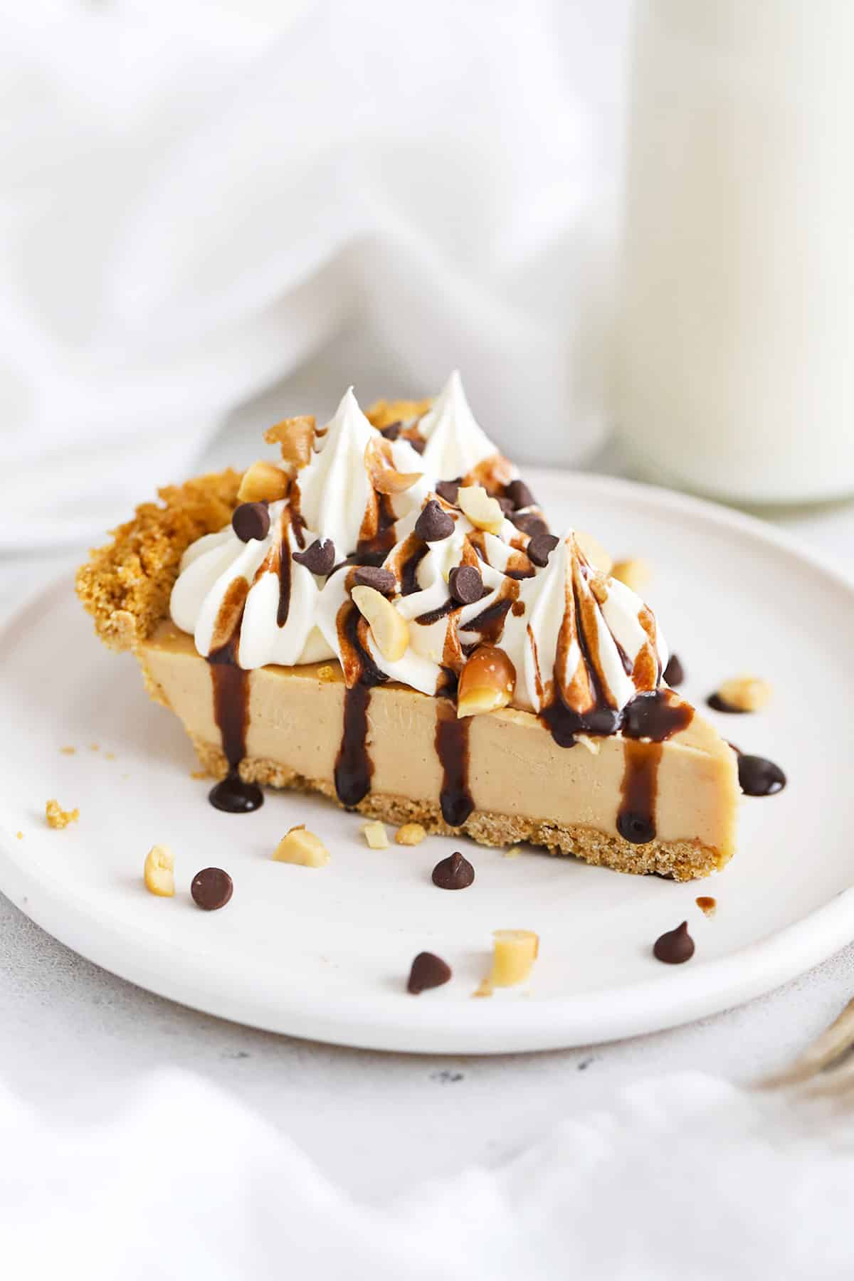 Front view of a slice of peanut butter pie with gluten-free graham cracker crust, whipped cream, and chocolate sauce