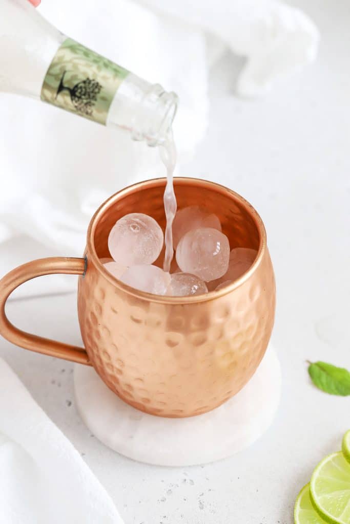Pouring ginger beer over ice to make a non-alcoholic moscow mule mocktail