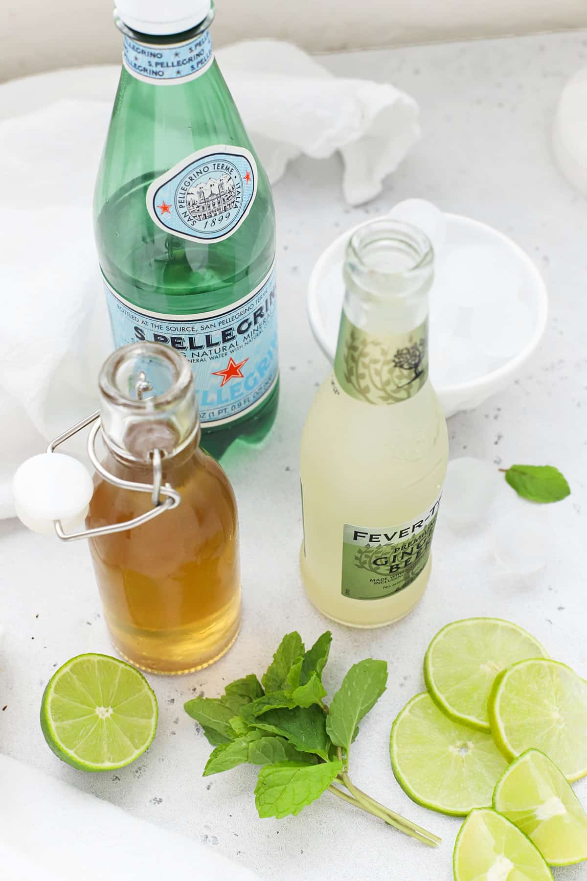 Front view of ingredients for a virgin moscow mule mocktail: ginger beer, mint, lime simple syrup, and sparkling water