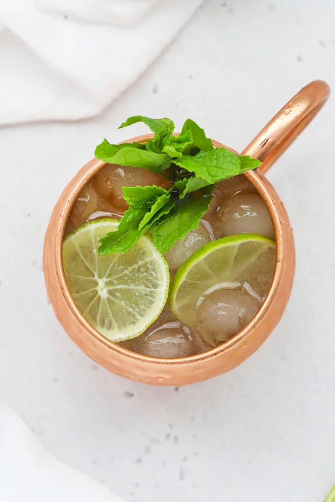 Overhead view of a moscow mule mocktail in a copper mug with lime slices and a sprig of fresh mint