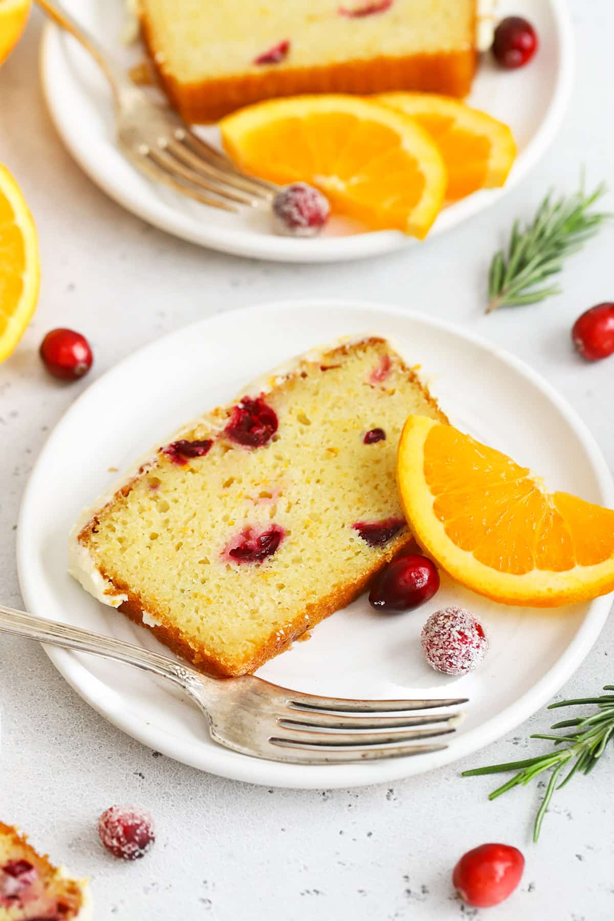 Front view of a slice of gluten-free orange cranberry loaf cake on a white plate with sugared cranberries