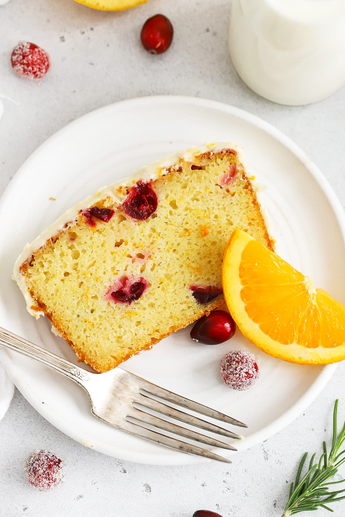 Overhead view of a slice of gluten-free orange cranberry loaf cake on a white plate with sugared cranberries