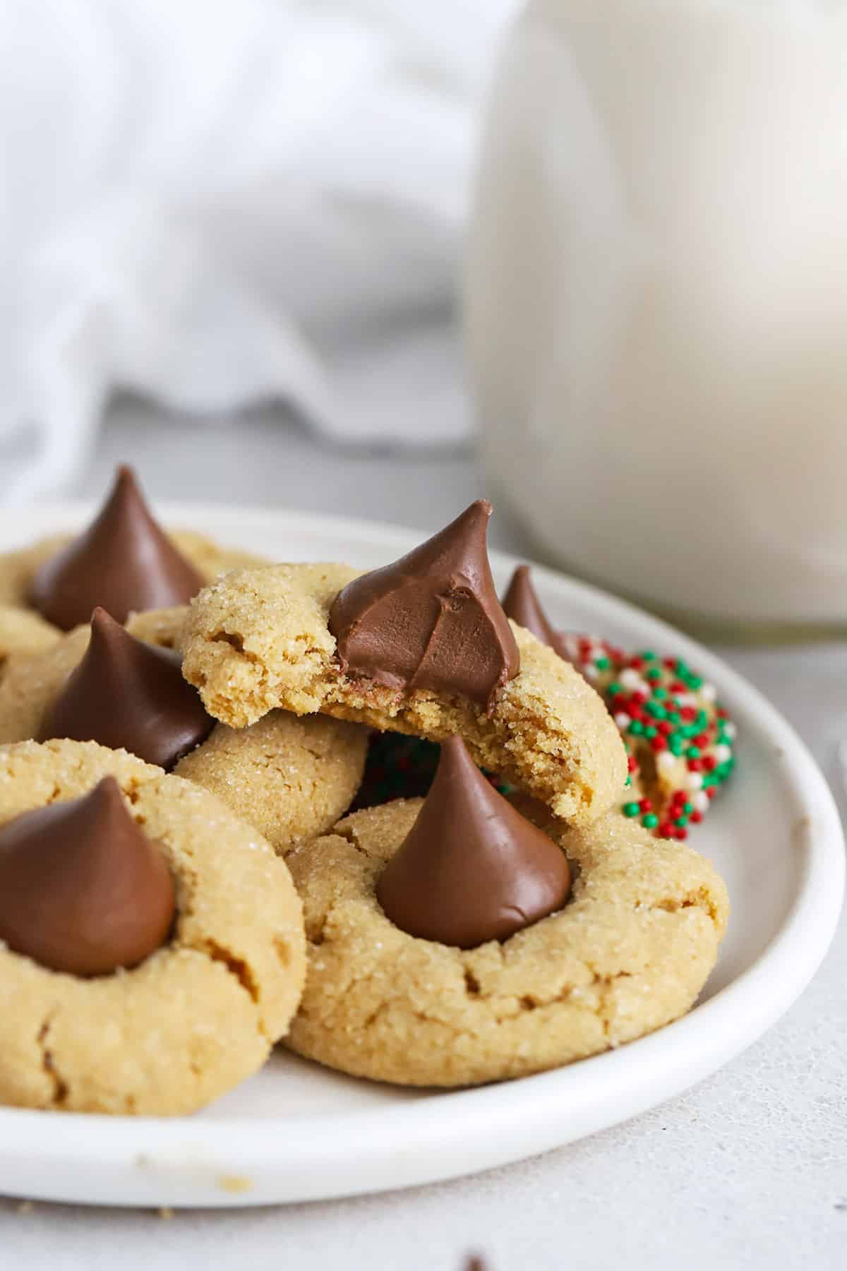 A plate stacked with gluten-free peanut butter blossom cookies. One has a bite out of it, revealing a soft, chewy texture.