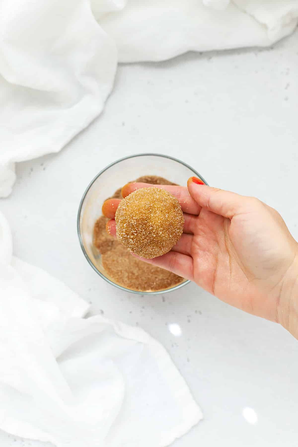 Rolling a ball of gluten-free pumpkin snickerdoodle cookie dough in cinnamon-sugar