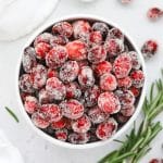 Overhead view of a bowl of sugared cranberries with a sprig of rosemary in the background