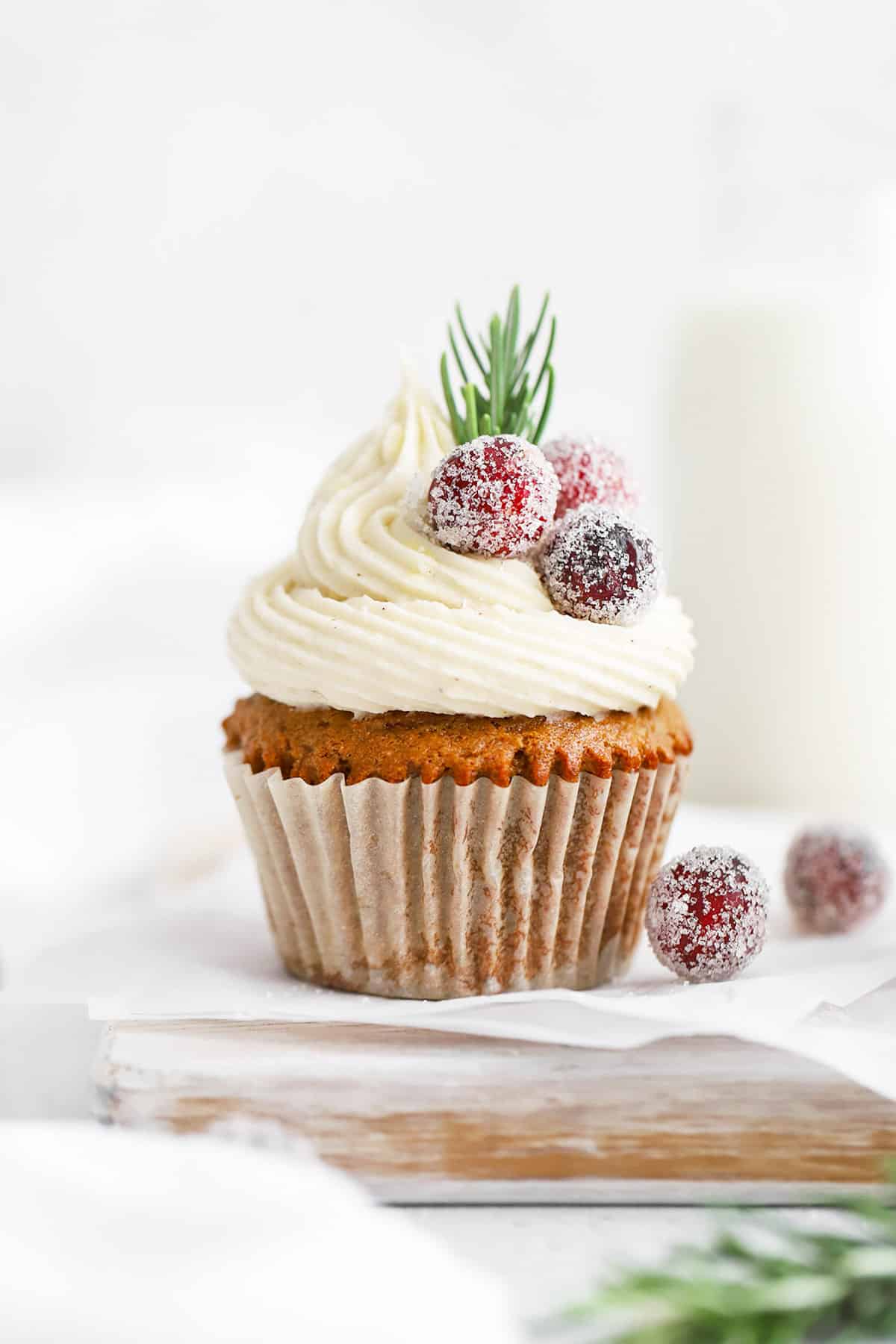 Front view of a gluten-free gingerbread cupcake topped with cream cheese, sugared cranberries, and rosemary