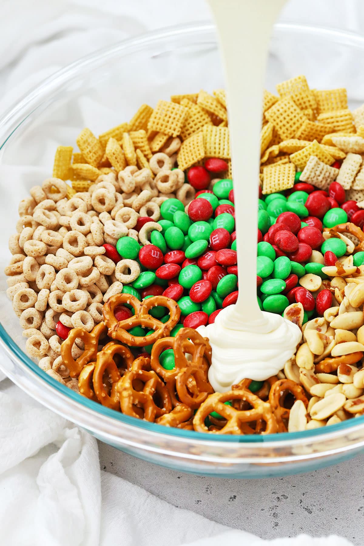 Pouring melted vanilla candy melts over cereal, pretzels, m&ms, and peanuts