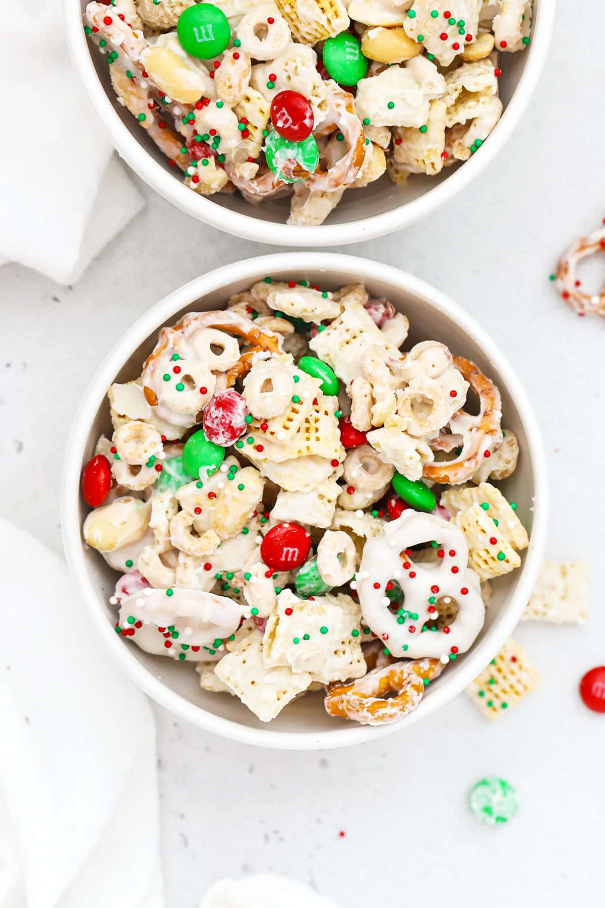 Two white bowls of gluten-free christmas chex mix with m&ms and pretzels