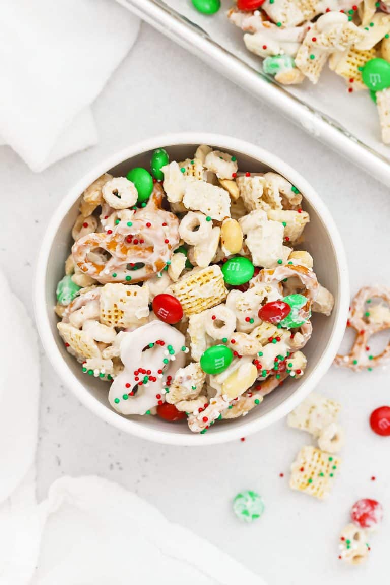 A white bowl of gluten-free christmas chex mix with m&ms and pretzels