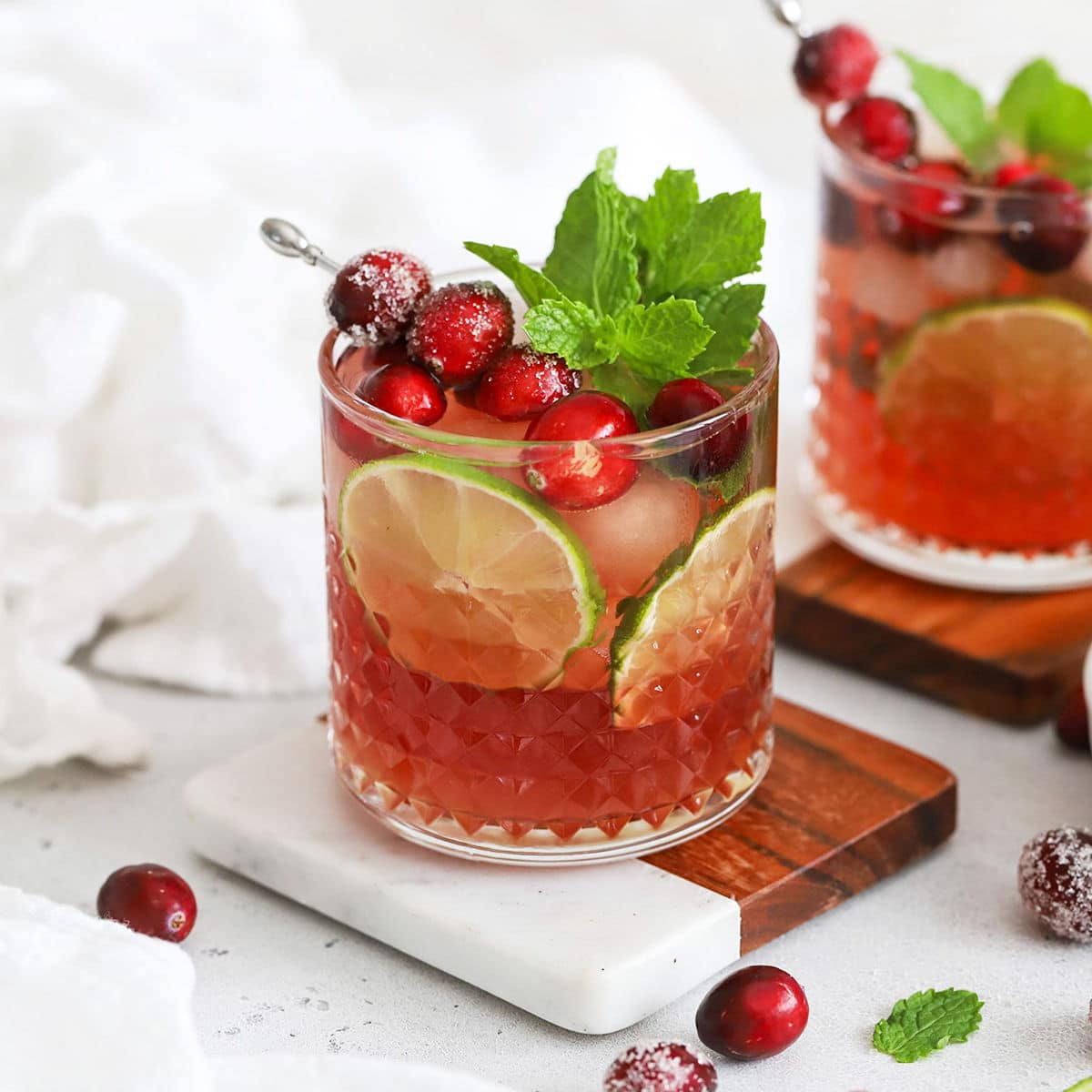 two cranberry lime mocktails in rocks glasses garnished with sugared cranberries and fresh mint