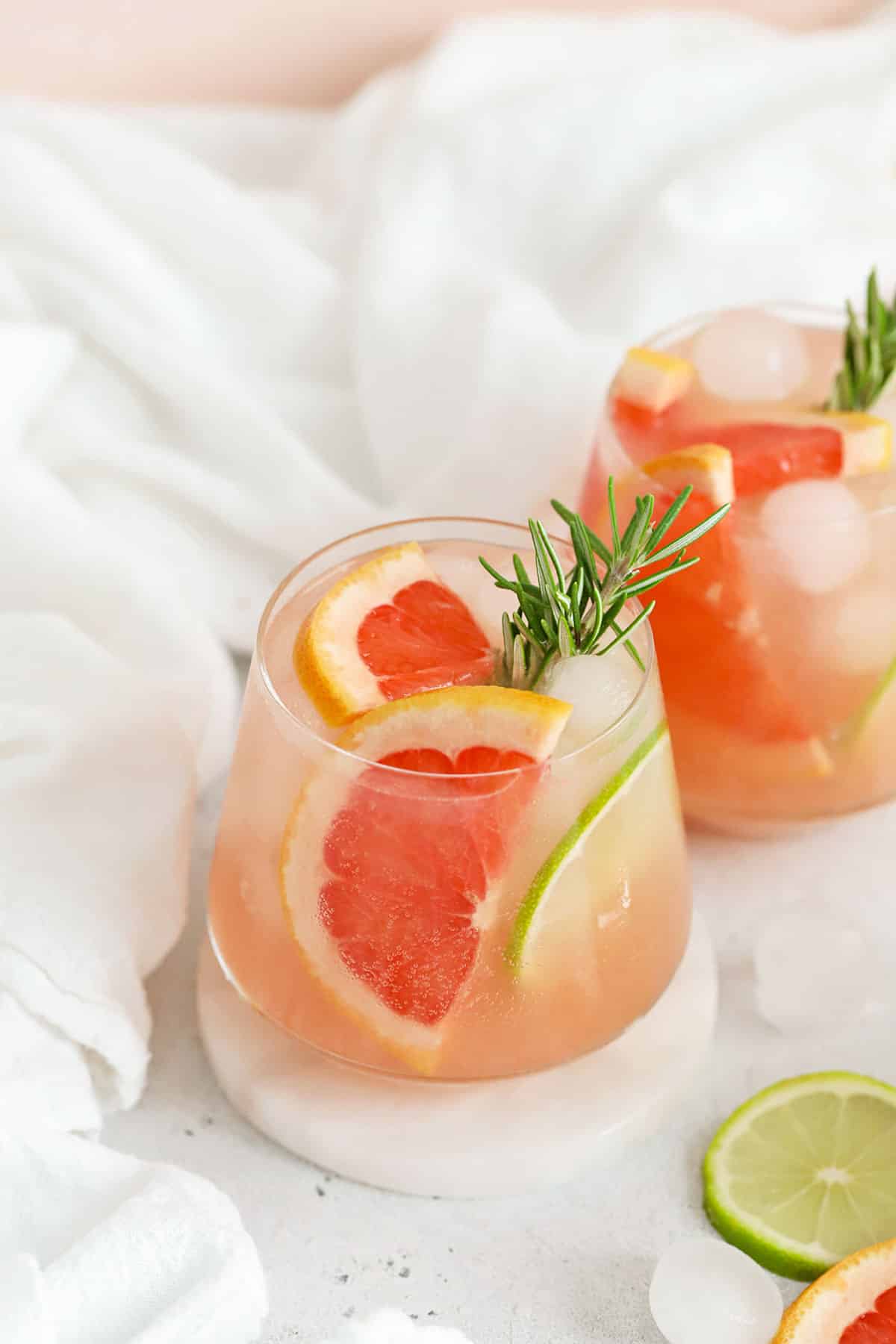 Two grapefruit mocktails garnished with grapefruit wedges, lime slices, and fresh rosemary
