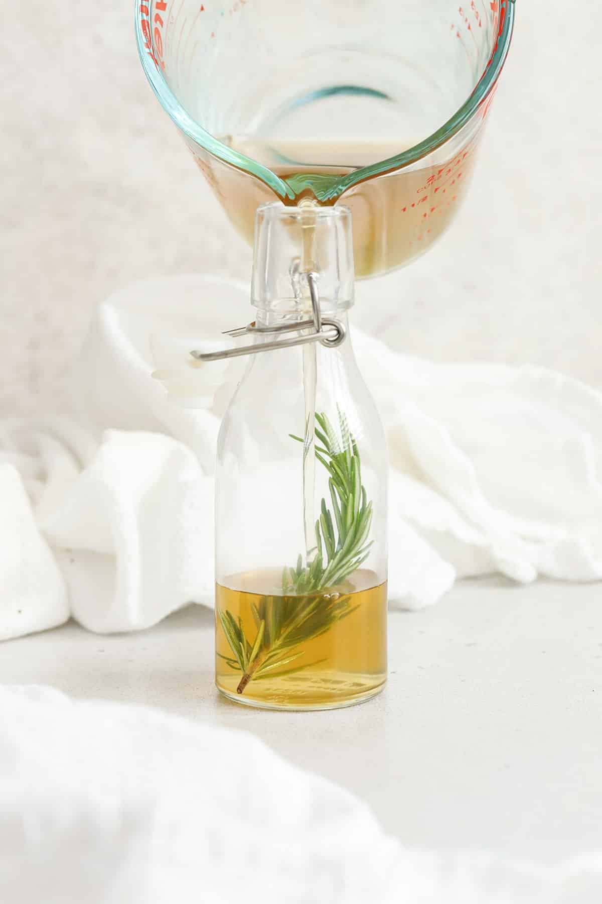Pouring rosemary simple syrup into a jar with a sprig of rosemary