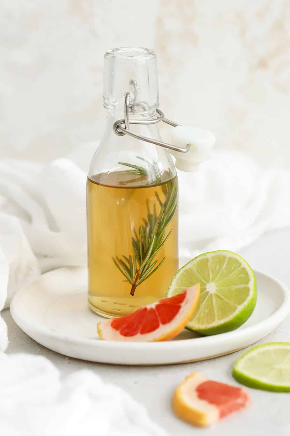 A small bottle of rosemary simple syrup on a plate with grapefruit and fresh lime