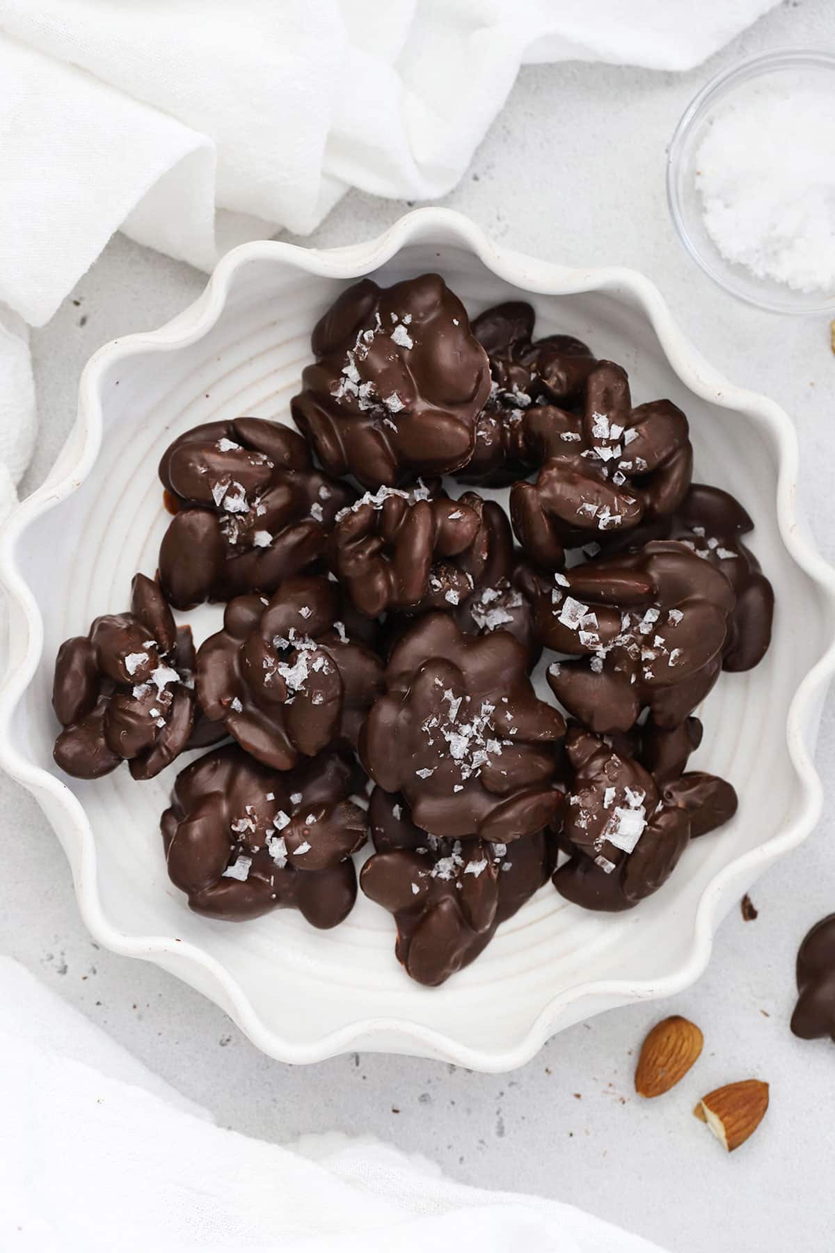 Dark chocolate almond clusters with flaky salt on a white ruffled plate