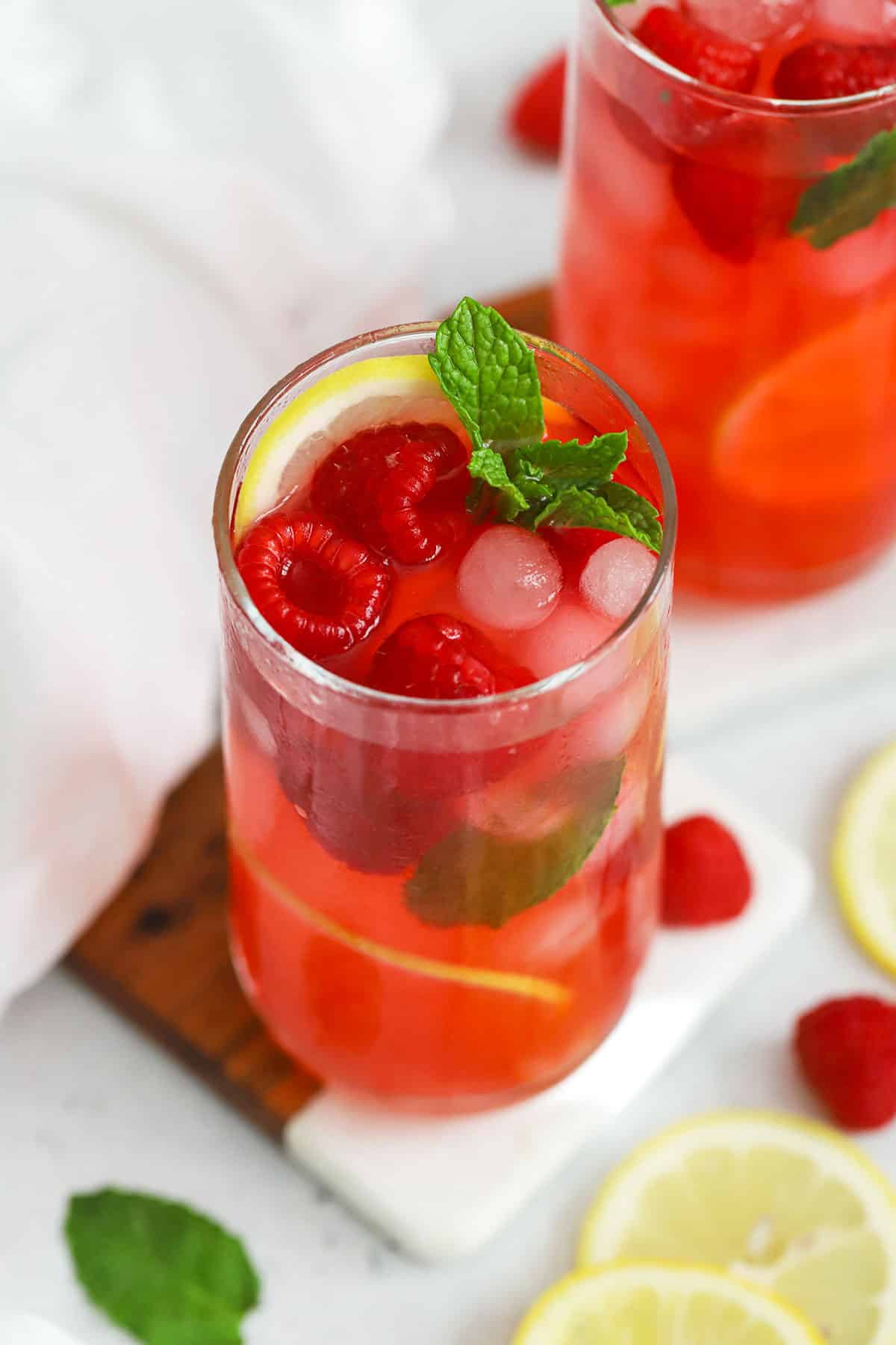 Two glasses of homemade raspberry lemonade with fresh raspberries, fresh mint, and lemon slices