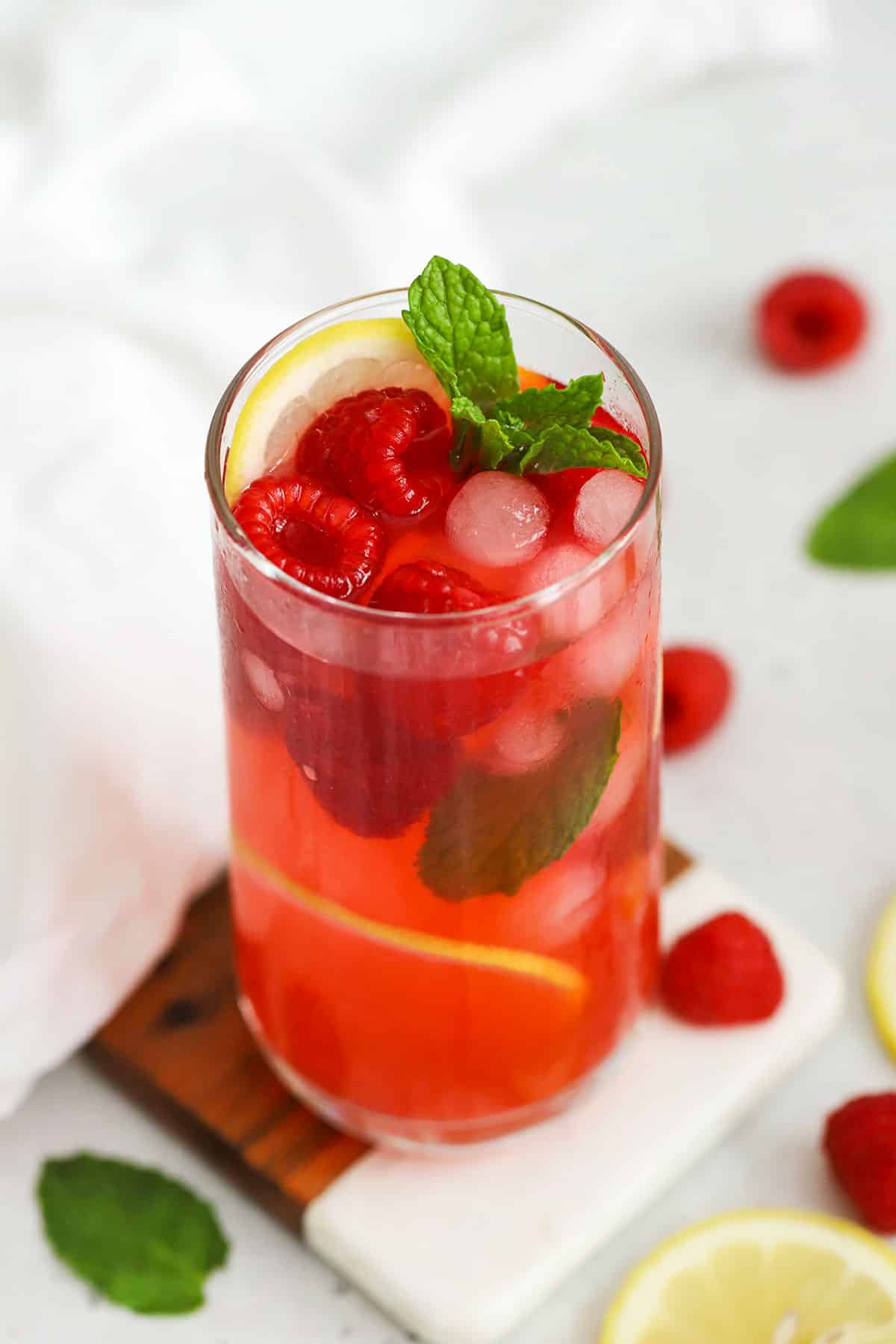 From scratch raspberry lemonade in a tall glass with lemon slices, raspberries, and fresh mint