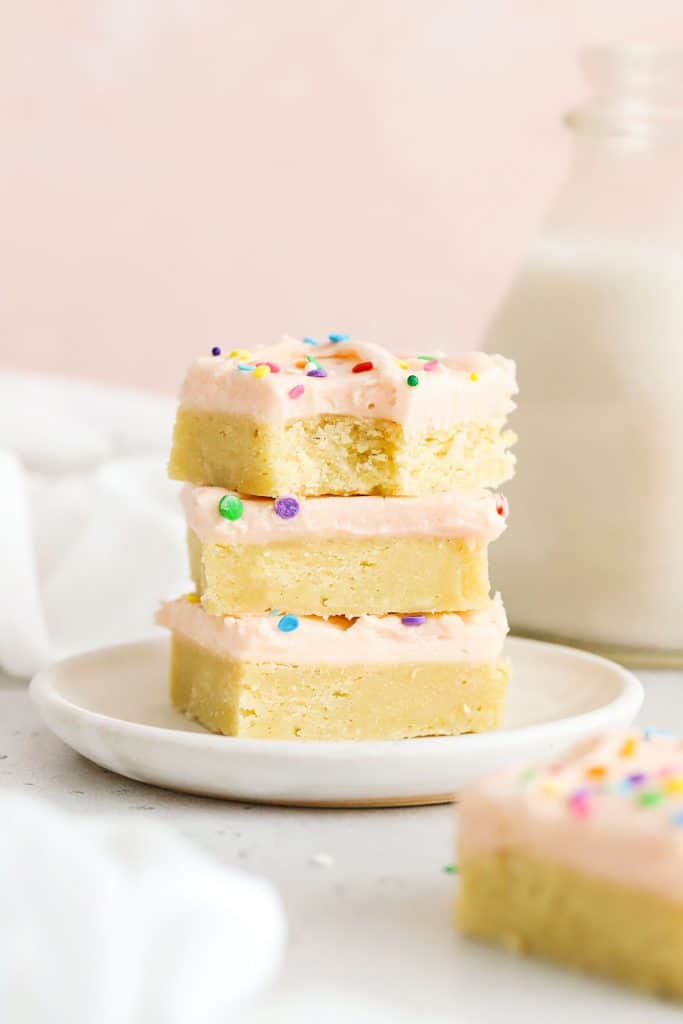 three sugar cookie bars with pink frosting stacked on a white plate