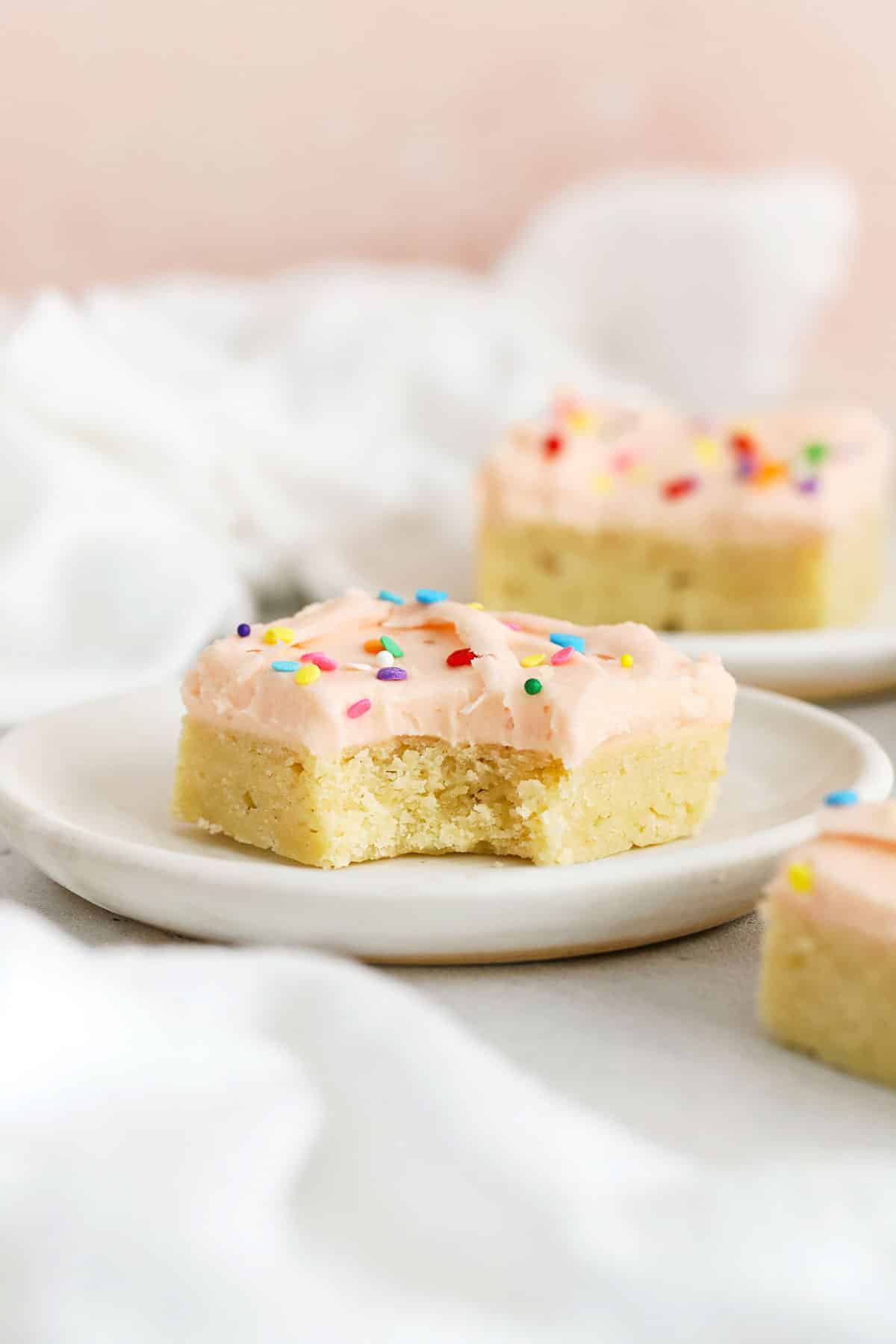 Gluten-free sugar cookie bars with pink frosting and sprinkles on white plates
