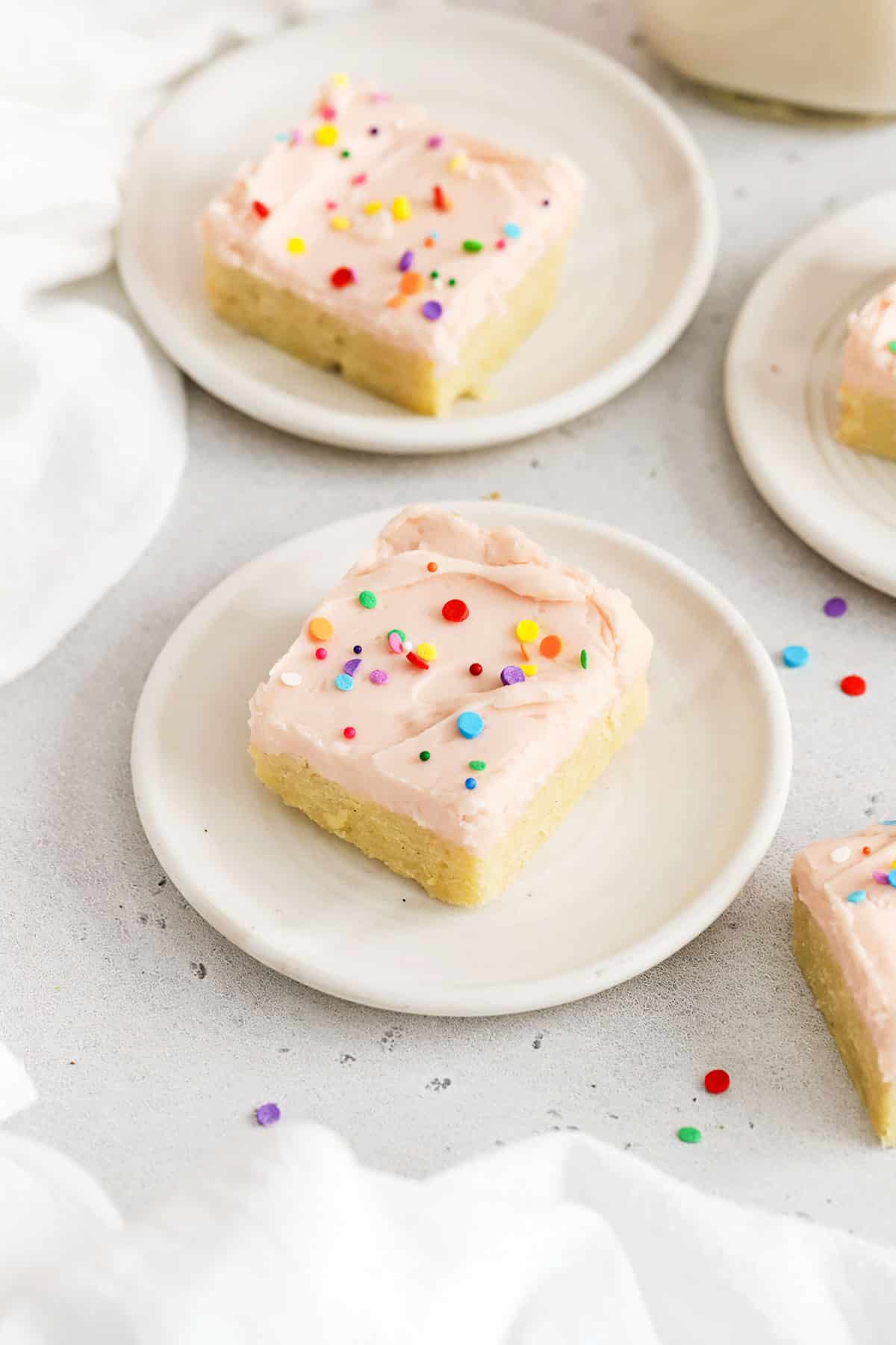 Gluten-free sugar cookie bars with pink frosting and sprinkles on white plates