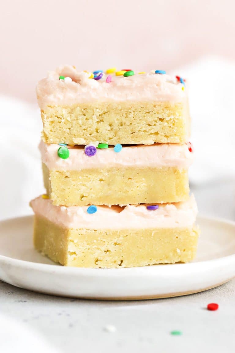 three sugar cookie bars with pink frosting stacked on a white plate