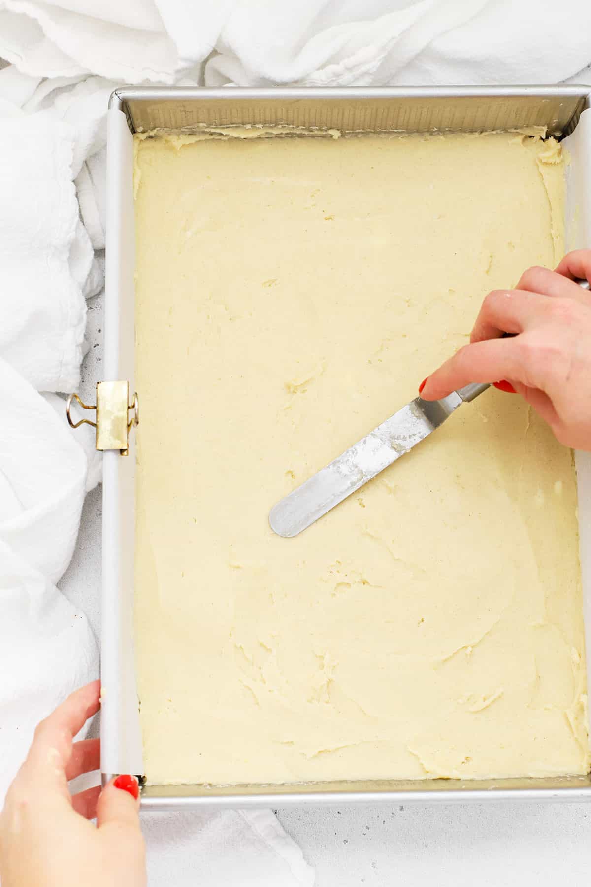 smoothing gluten-free sugar cookie dough out into an 9x13 pan with an offset spatula