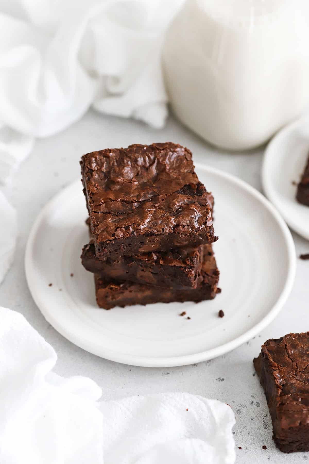 three fudgy gluten-free vegan brownies stacked on a white plate